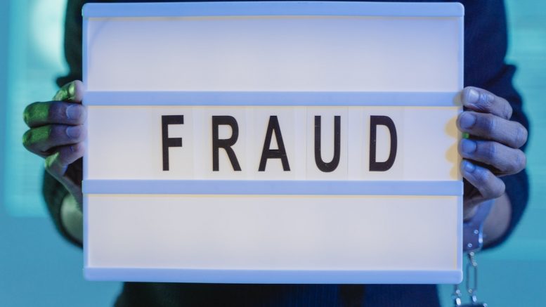 A Person with Handcuffs Holding a Sign that Says Fraud